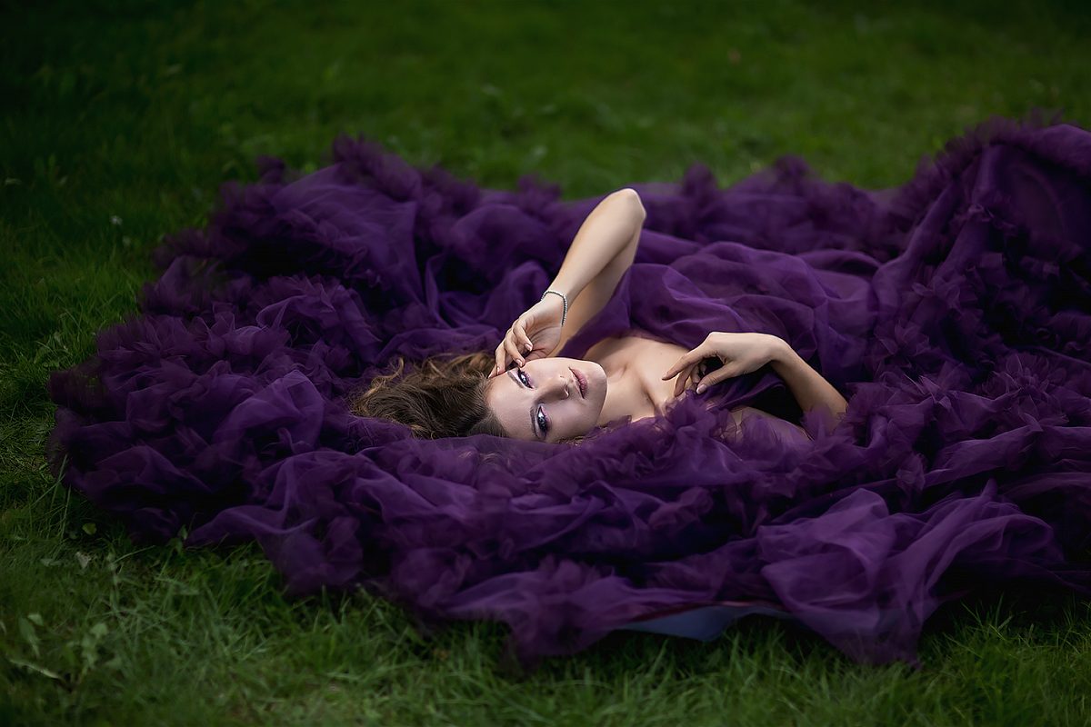 Woman lying on grass in a voluminous purple dress