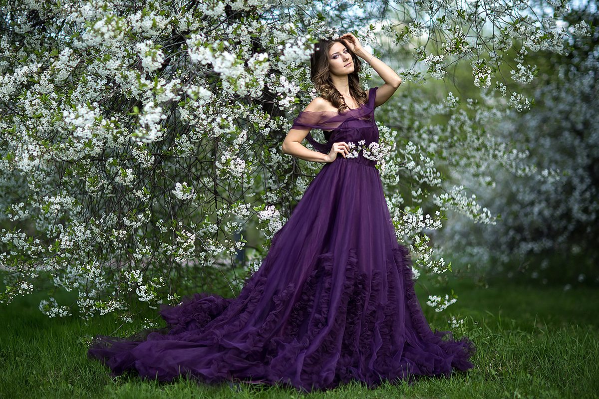 Woman in a long purple dress beneath blooming trees