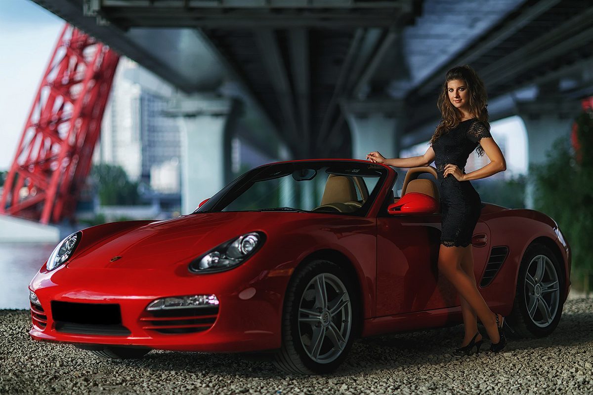 Woman in a black dress beside a red convertible