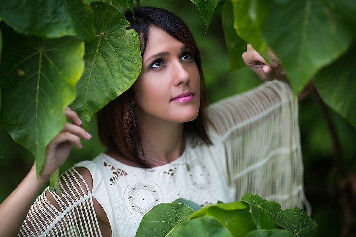 Portrait of a woman in a white blouse among large leaves