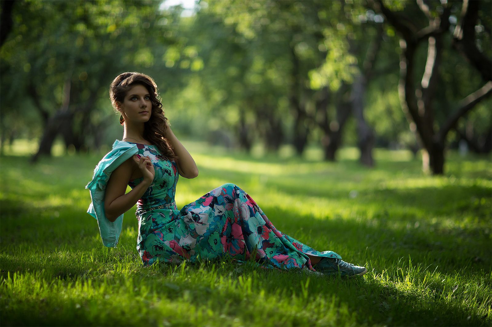 Woman in a floral dress sitting on grass in a park
