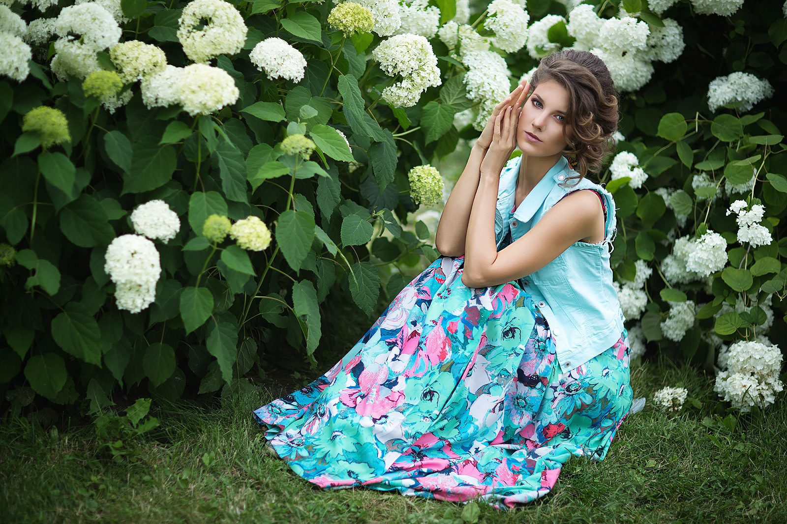 Woman in a floral dress sitting beside a blooming shrub