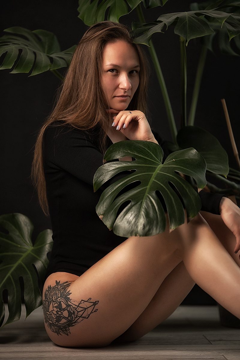 Woman in a black bodysuit sitting among monstera leaves
