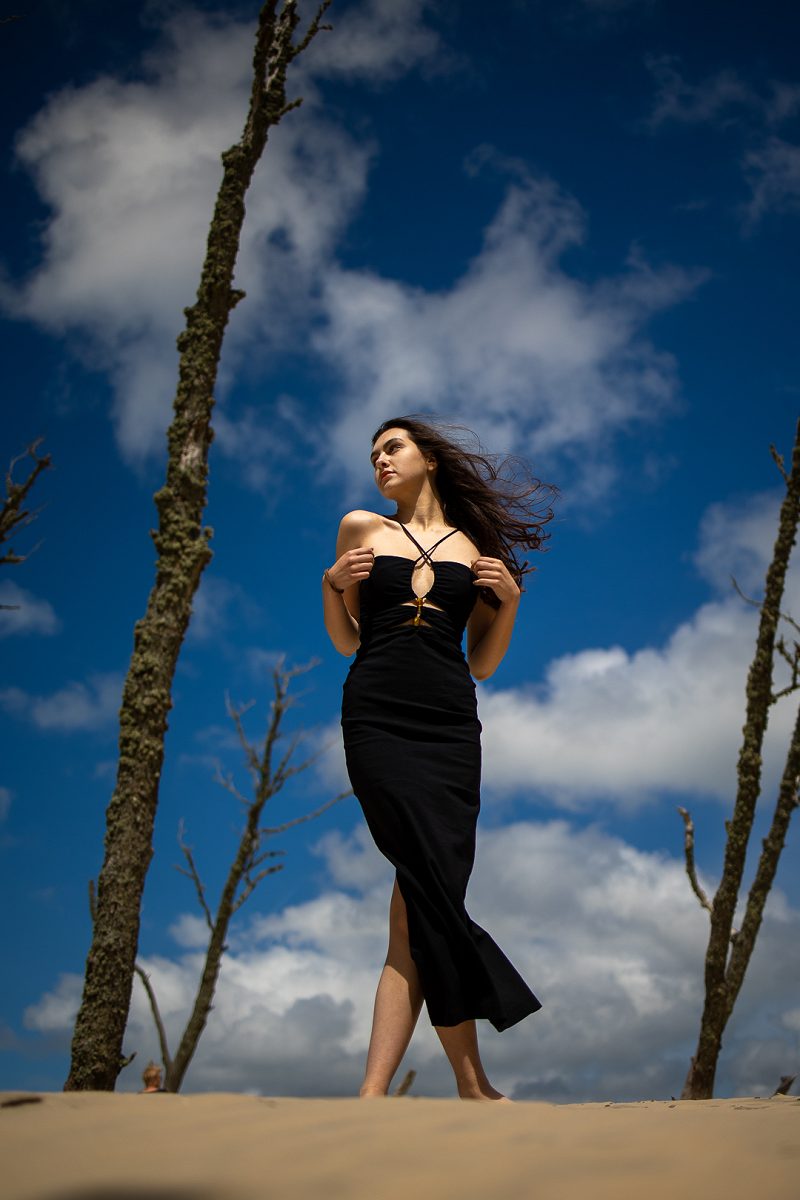 Woman in a black dress walking on sand under a blue sky