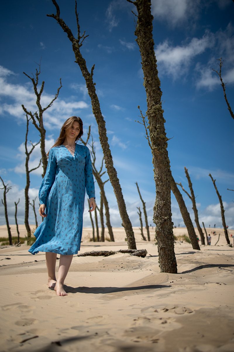 Woman in a blue dress among trees on a sandy shore